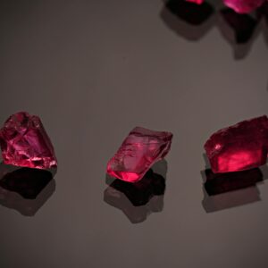 Three red gemstones glitter against a dark reflective background in a still life composition.