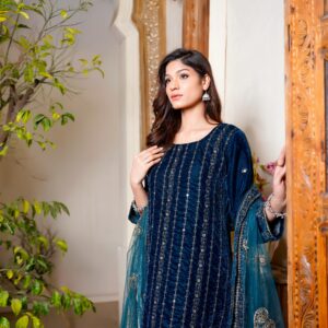 Fashion model in a blue velvet dress posing near intricate wooden carvings in Lahore, Pakistan.